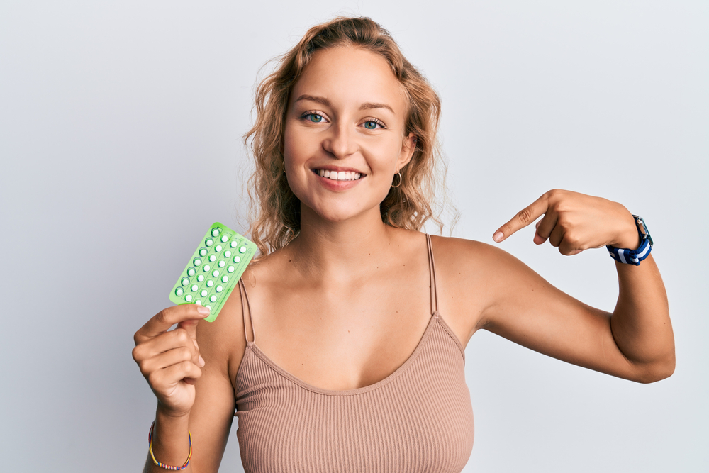Beautiful caucasian woman holding birth control pills pointing finger to one self smiling happy and proud 