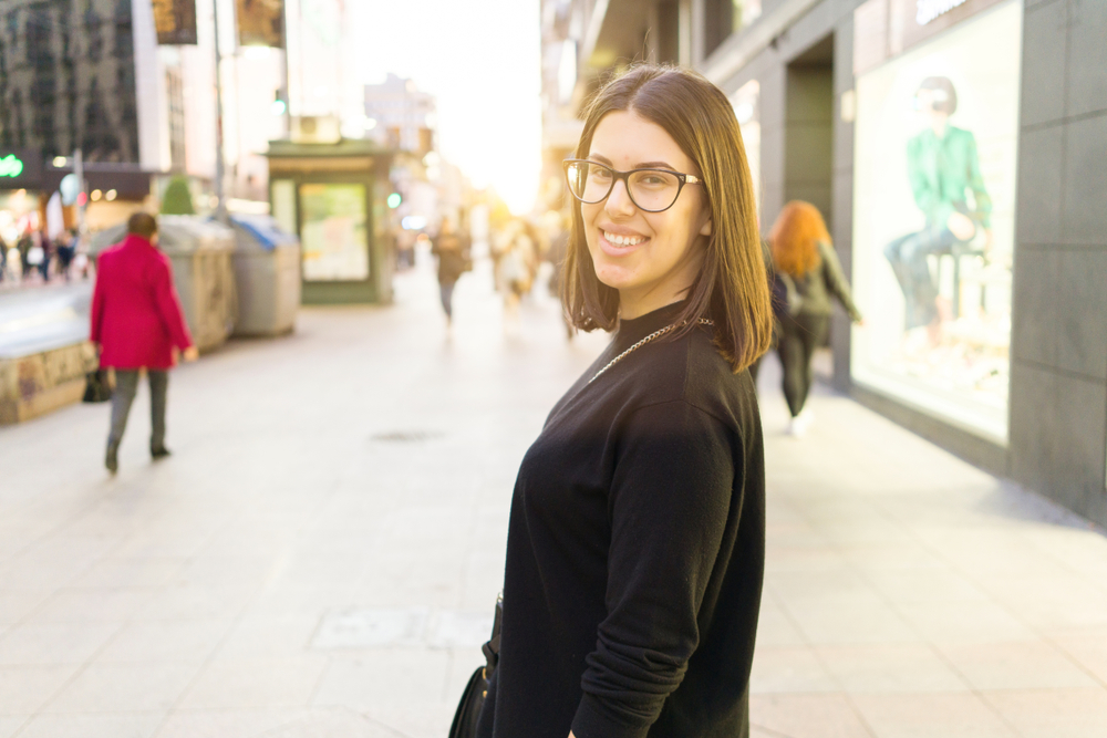 Beautiful young brunette woman smiling excited walking down the city streets, happy and confident expression standing outdoors at the town