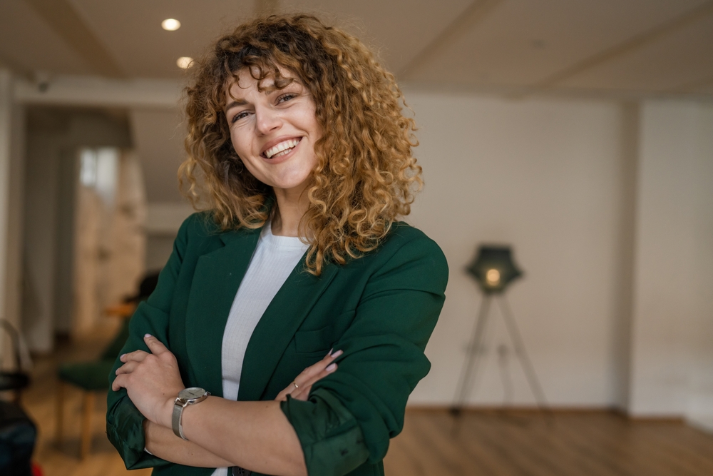 Smiling professional woman with curly hair standing with arms crossed in a modern indoor setting, reflecting confidence, balance, and personalized hormone therapy care – bioidentical hormones miami fl
