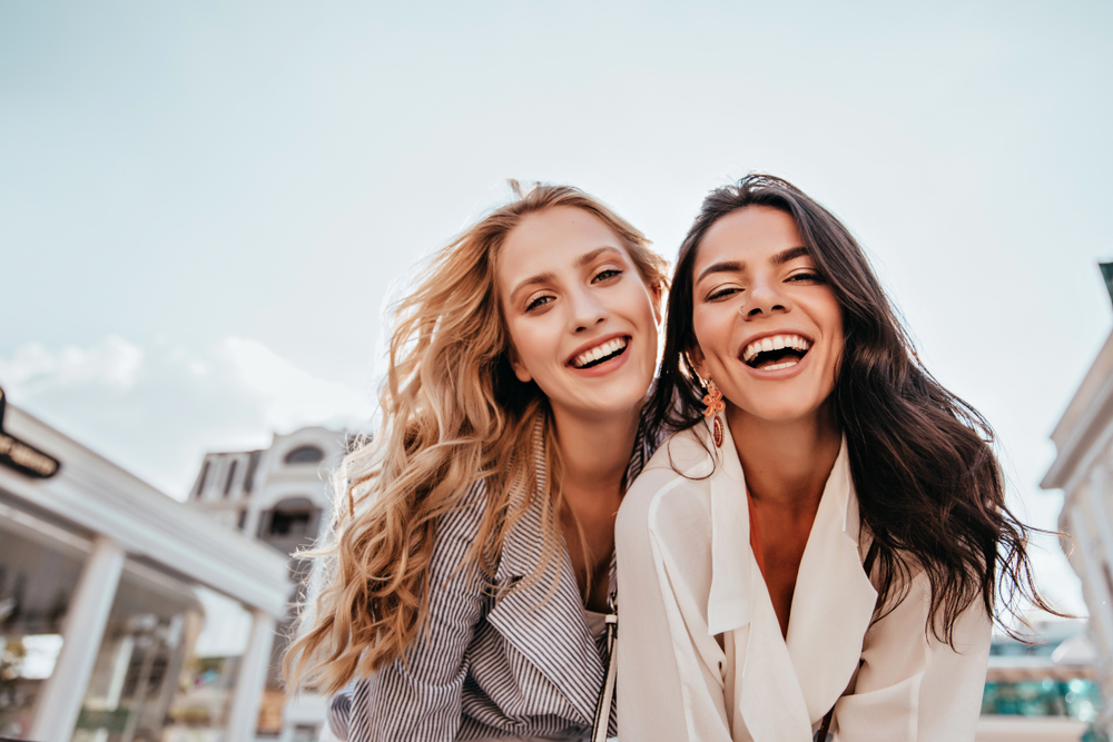 Two happy women laughing together in a bright outdoor setting, symbolizing confidence, satisfaction, and patient-centered care associated - sidiq aldabbagh