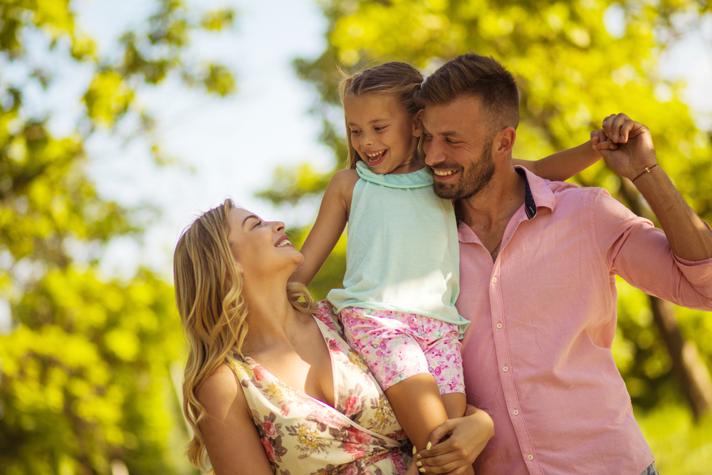 Happy family enjoying time together outdoors representing holistic women’s healthcare – gynecologist homestead fl Smiling parents lifting their young daughter in a sunny park, symbolizing family-centered care, trust, and comprehensive women’s health services – gynecologist homestead fl