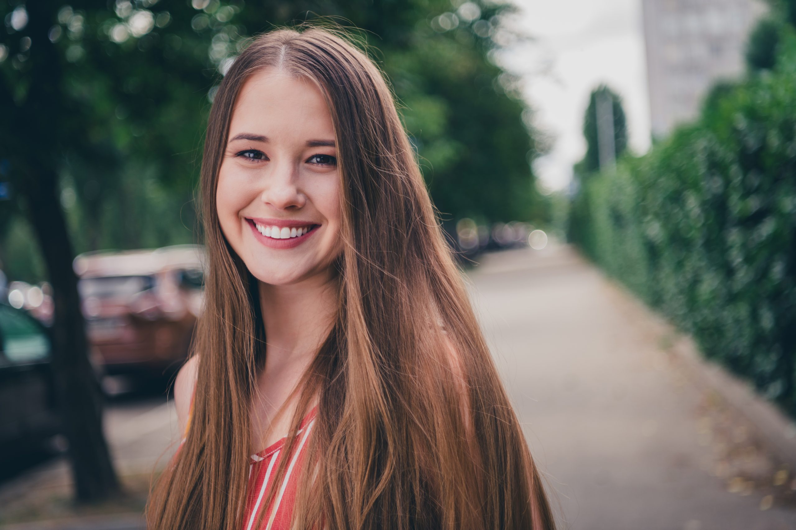 Smiling young woman outdoors representing confidence and approachable women’s healthcare – gynecologist homestead fl Happy young woman smiling while standing on a tree-lined street, reflecting confidence, comfort, and compassionate care - gynecologist homestead fl