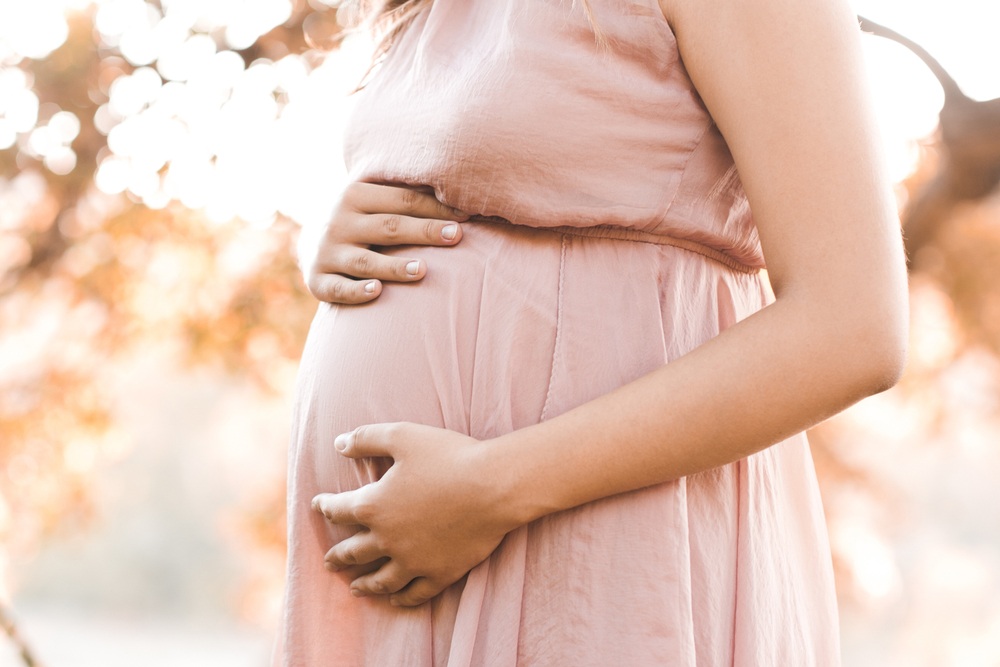 Close-up of an expectant mother’s hands resting on her pregnant belly outdoors, symbolizing nurturing care, hormonal balance, and personalized women’s health support – bioidentical hormones miami fl