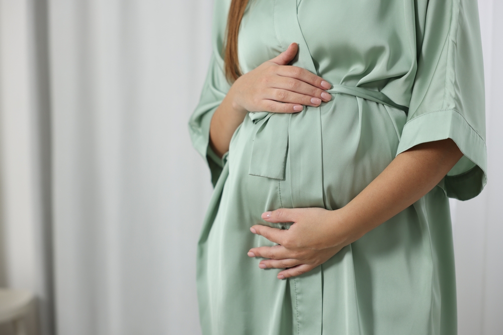 Pregnant woman gently holding her belly while wearing a soft green robe, symbolizing prenatal care, comfort, and maternal wellness – trusted women’s health center