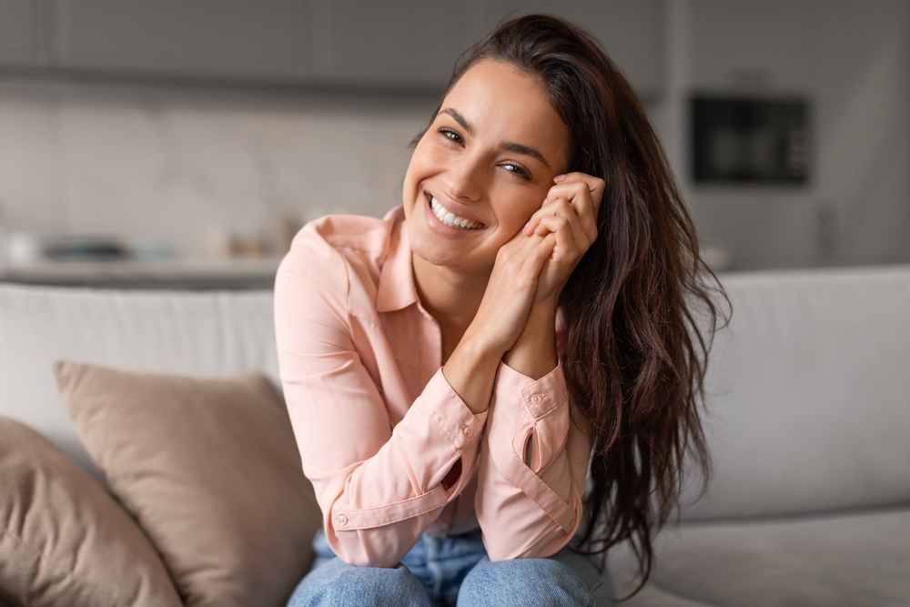 Woman smiling warmly while seated on a sofa in a cozy indoor setting, reflecting trust, comfort, and compassionate women’s healthcare – obgyn deerfield beach