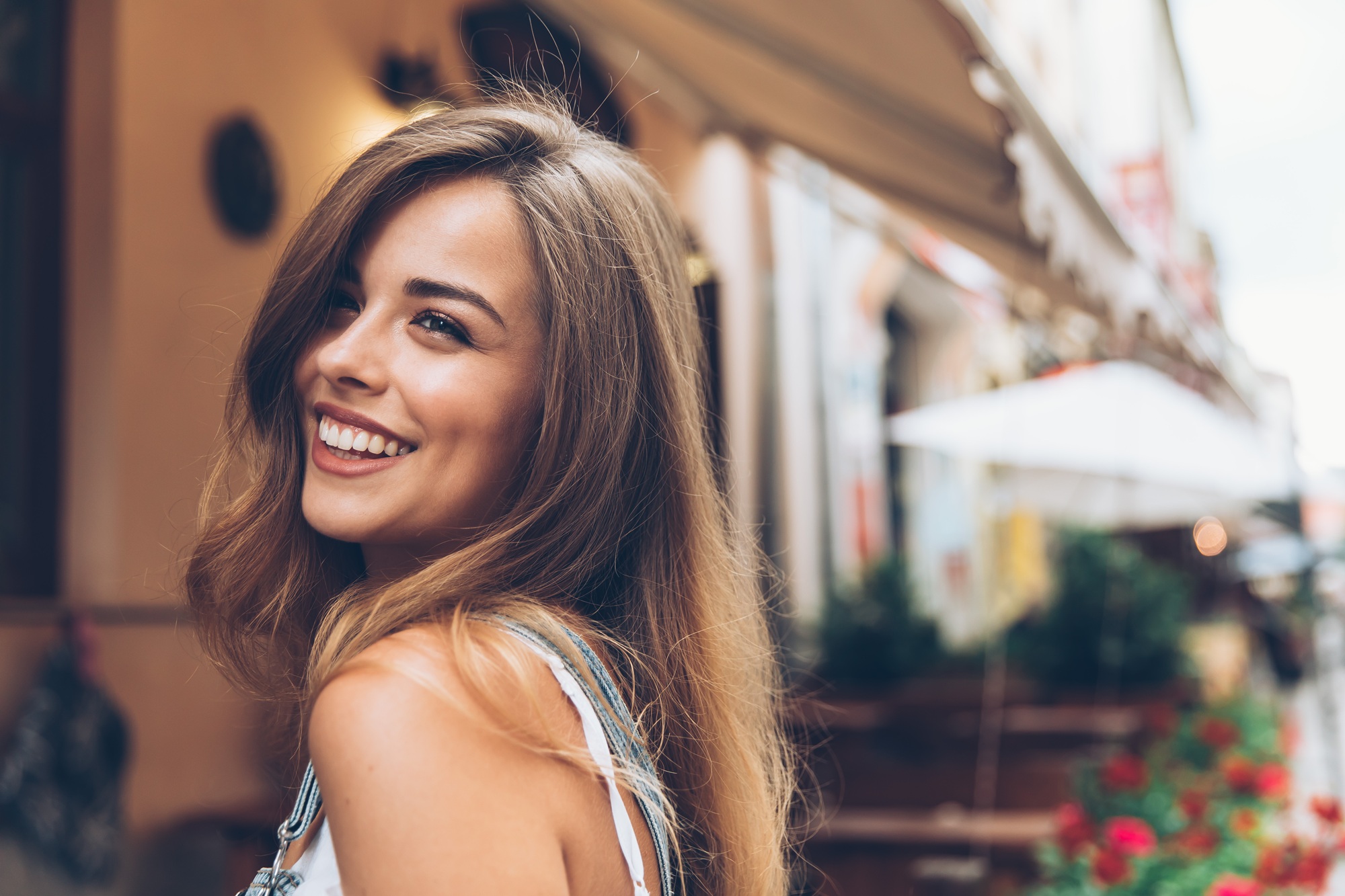 Happy woman smiling over her shoulder while walking along a café-lined street, reflecting comfort, confidence, and compassionate women’s healthcare – obgyn deerfield beach