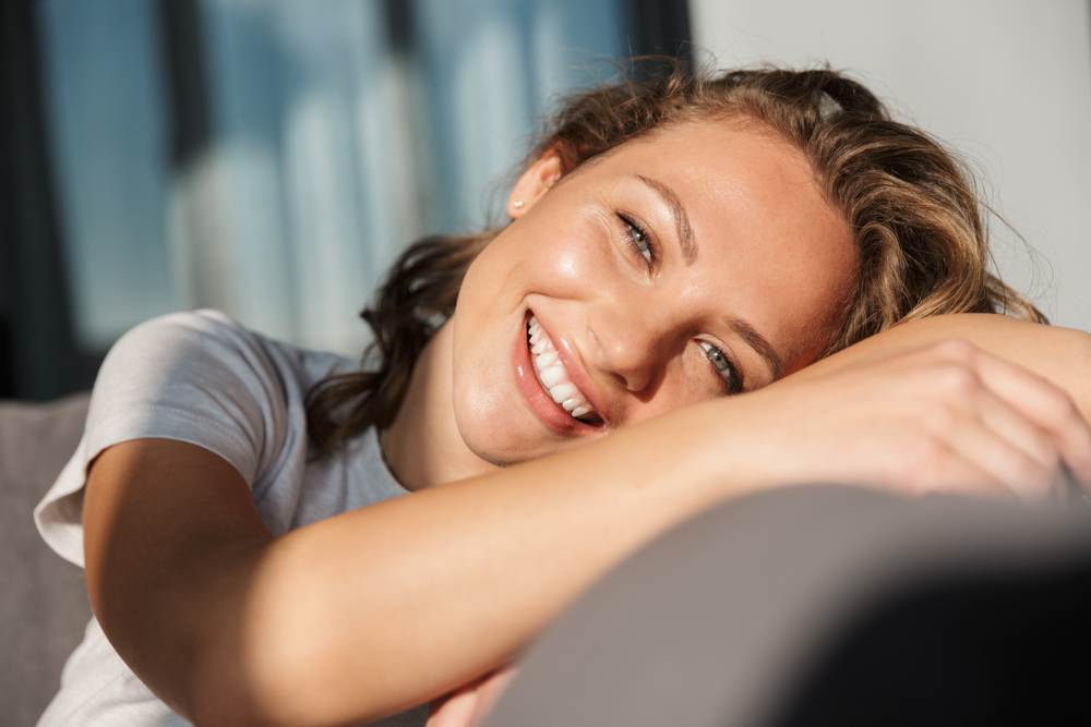 Relaxed woman smiling while resting her head on her arm in soft natural light, symbolizing comfort, emotional well-being, and personalized hormone therapy care – bioidentical hormones miami fl