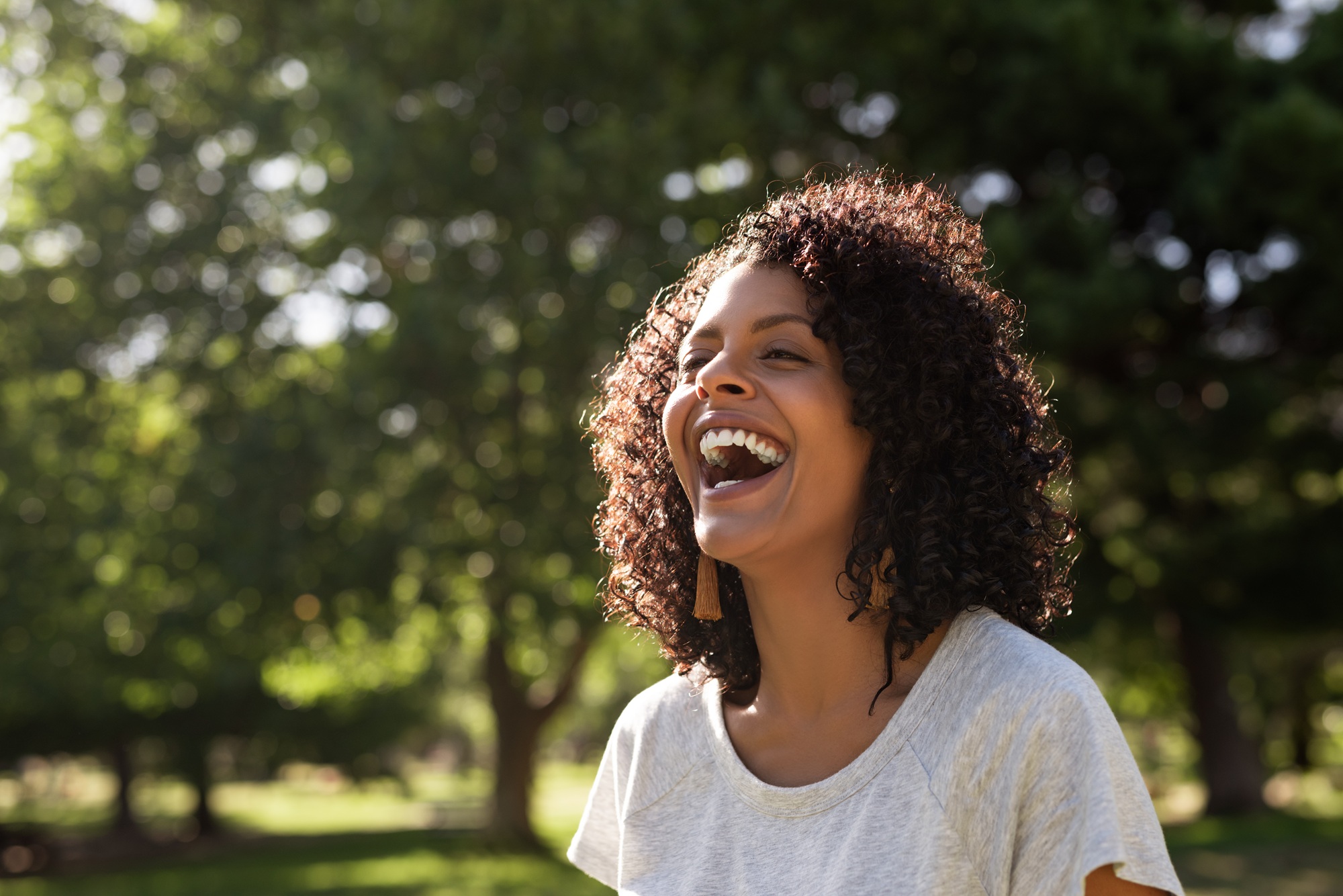 Happy woman with curly hair laughing in a sunny park, reflecting vitality, comfort, and supportive women’s healthcare – obgyn north miami beach