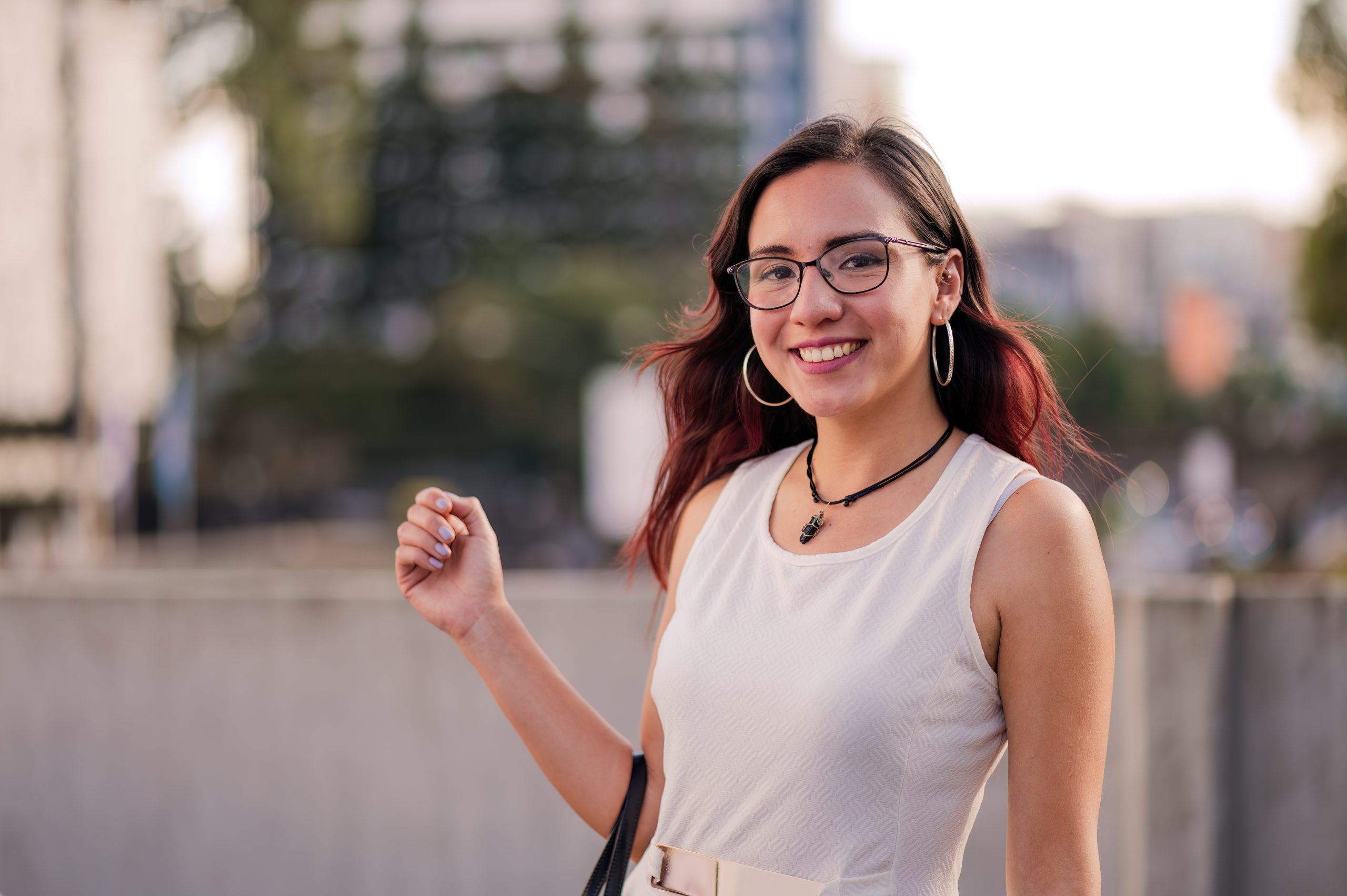 Smiling woman wearing glasses walking outdoors in an urban setting, reflecting confidence, approachability, and quality care provided - obgyn hialeah