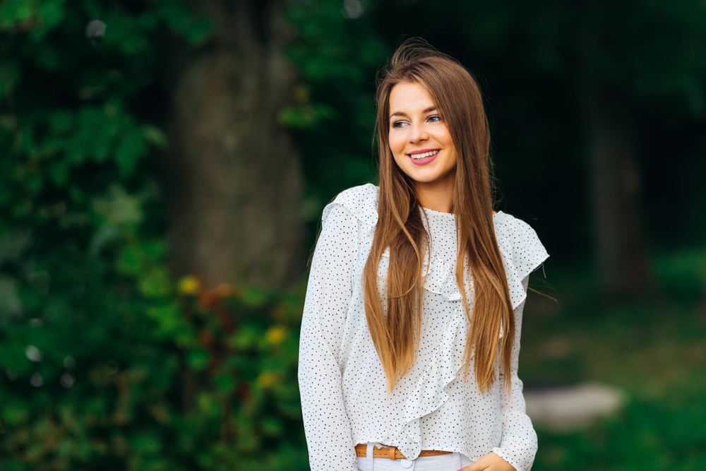 Young woman smiling confidently while standing in a green outdoor environment, reflecting wellness and compassionate care - trusted women’s health center