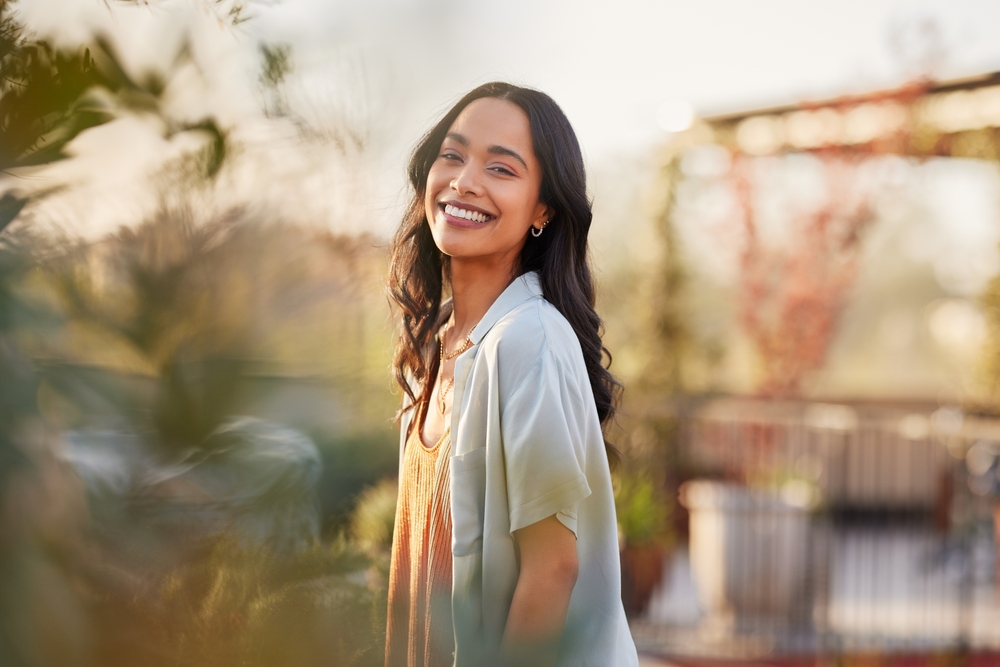 Happy woman smiling in a sunlit outdoor setting with soft greenery, representing vitality, balance, and personalized hormone therapy care – bioidentical hormones miami fl