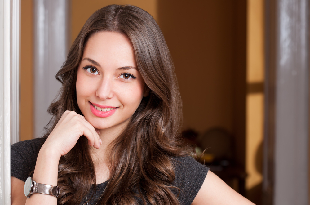 Smiling woman with long hair resting her chin on her hand in a warm indoor setting, reflecting confidence, comfort, and patient-centered care – obgyn margate