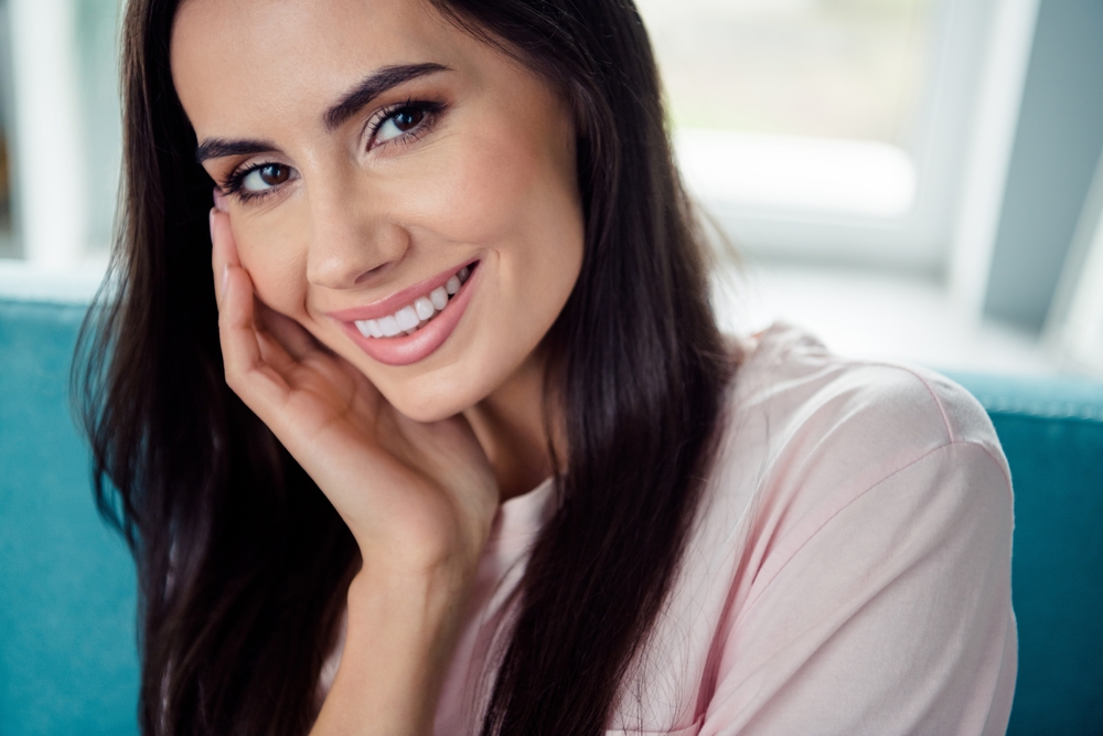 Smiling woman in a calm, welcoming indoor setting representing personalized care – delray obgyn Close-up of a smiling woman resting her face on her hand, reflecting comfort, confidence, and patient-focused women’s healthcare – delray obgyn