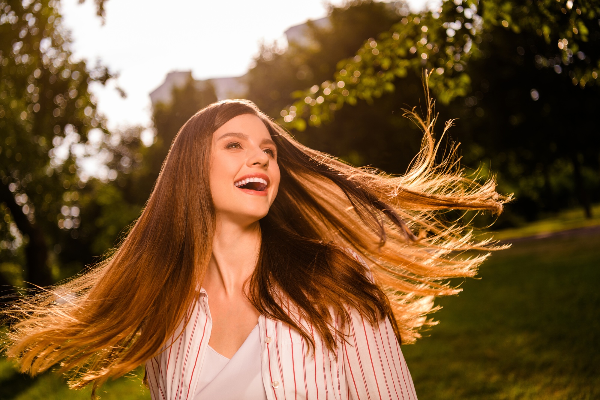 Smiling woman enjoying fresh air and natural movement in a green outdoor setting – obgyn doral Happy young woman with flowing hair smiling outdoors in a sunlit park, representing vitality, confidence, and compassionate women’s healthcare – obgyn doral
