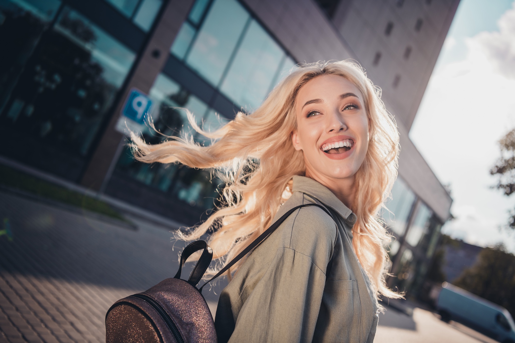 Happy woman with flowing hair carrying a backpack while walking outdoors, symbolizing confidence, approachability, and positive patient impressions – sidiq aldabbagh photos