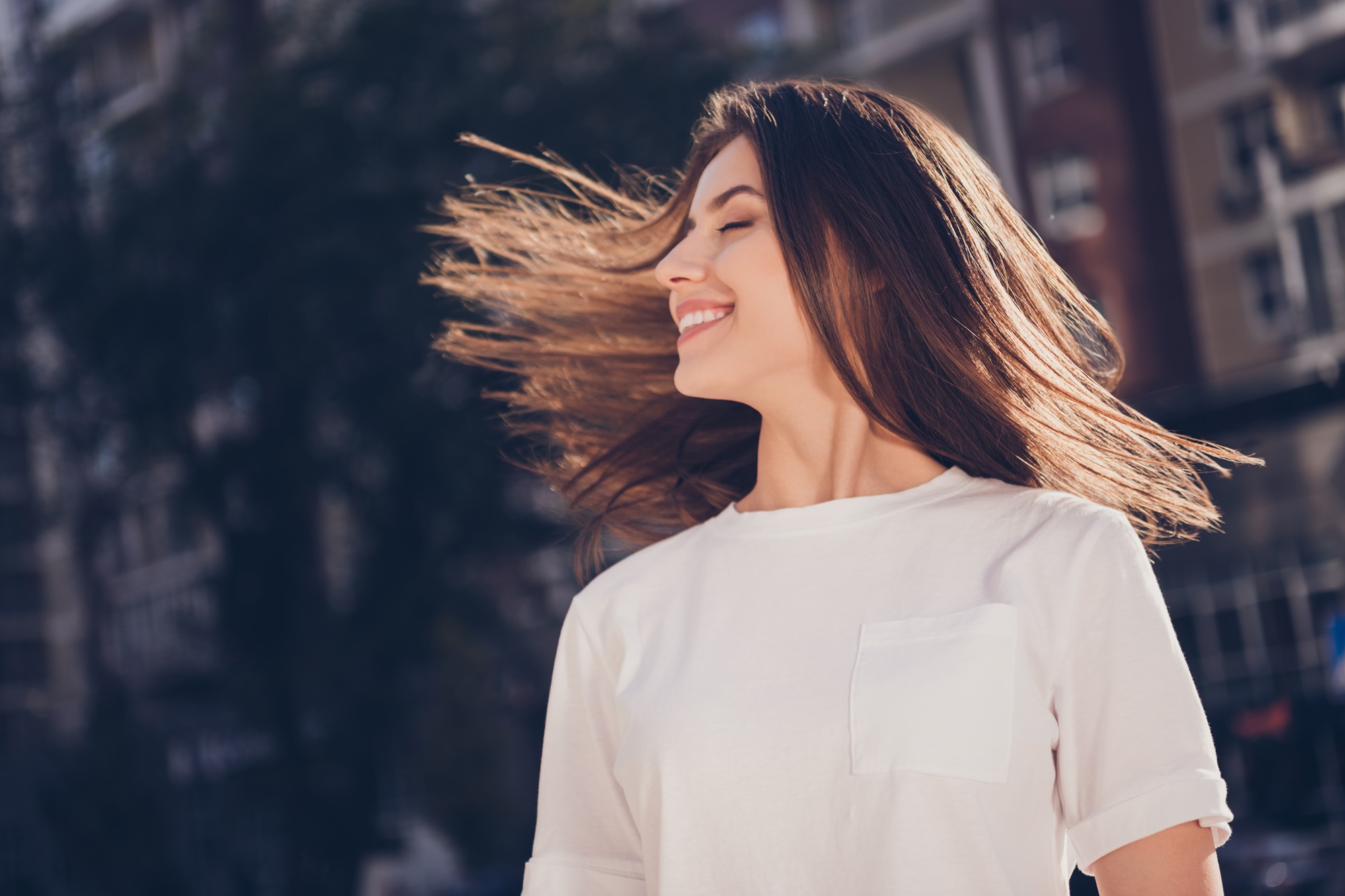 Woman smiling and enjoying movement outdoors representing confidence and vitality – obgyn doral Young woman smiling as her hair moves in the breeze in an urban outdoor setting, symbolizing freedom, confidence, and patient-centered women’s healthcare – obgyn doral