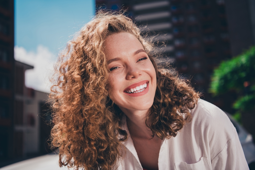 Happy young woman smiling in natural light outdoors, representing confidence, positivity, and patient-centered care – pompano beach clinic