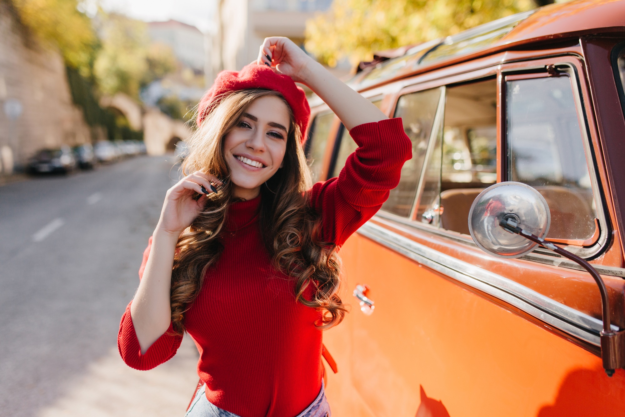 Smiling woman enjoying a bright outdoor moment reflecting confidence and wellness – obgyn pompano beach fl Happy woman wearing a red sweater and hat standing beside a classic car on a sunny street, representing confidence, positivity, and patient-focused women’s healthcare – obgyn pompano beach fl