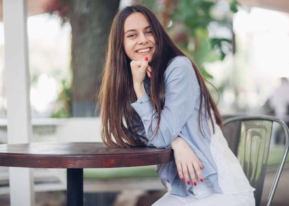 Confident woman smiling while seated at an outdoor table, representing comfort, wellness, and patient - trusted women’s health center
