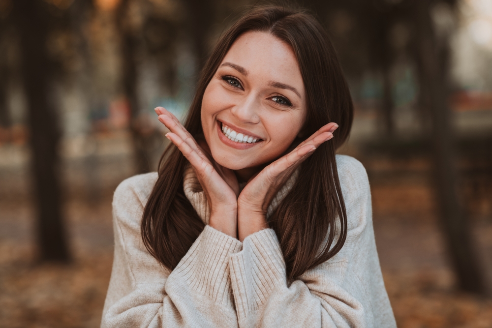 Smiling woman outdoors with hands framing her face, representing confidence, wellness, and compassionate care – trusted women’s health center