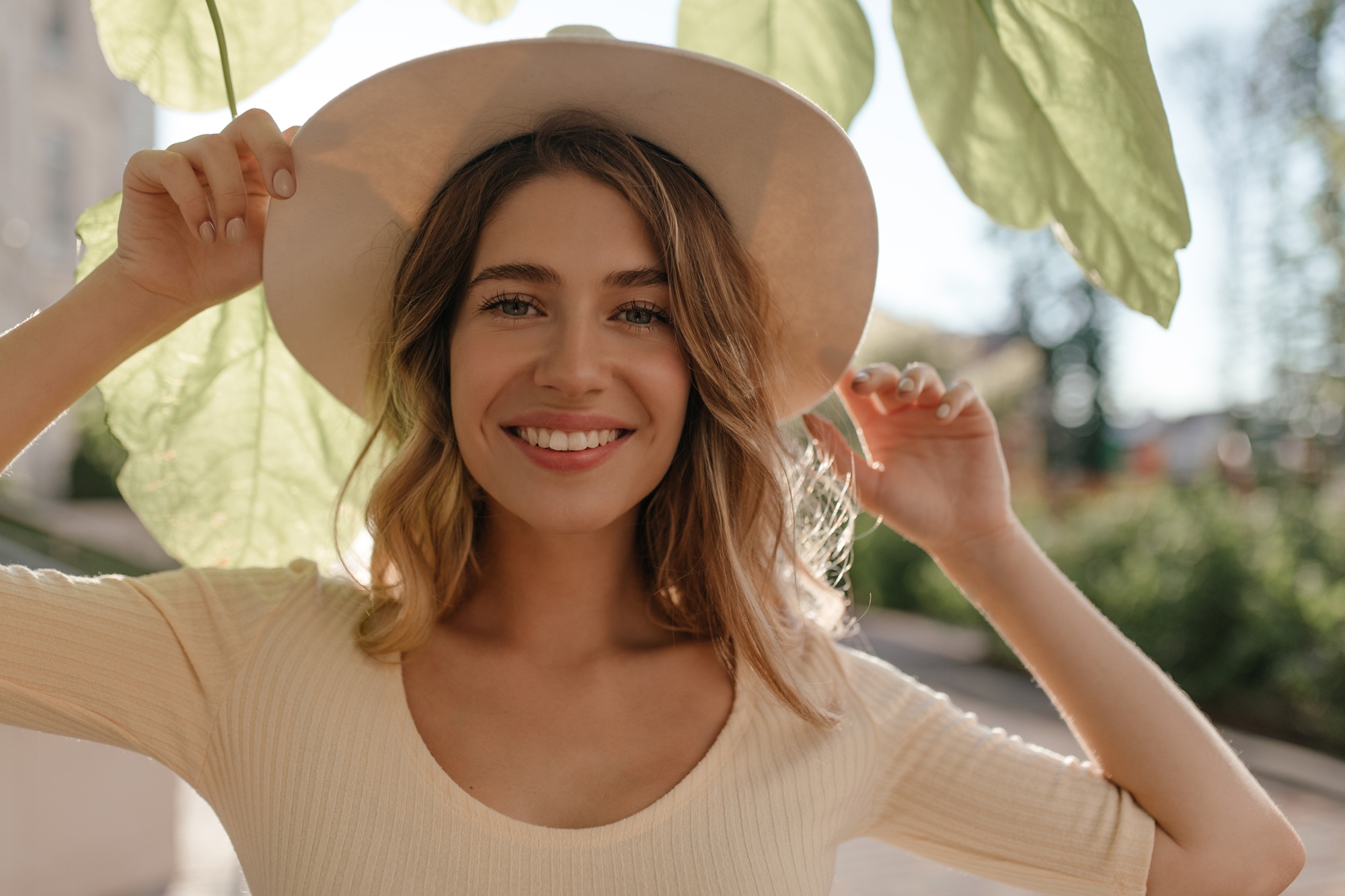 Happy woman smiling while adjusting her hat in a sunlit outdoor setting, reflecting comfort, confidence, and approachable women’s healthcare – obgyn deerfield beach