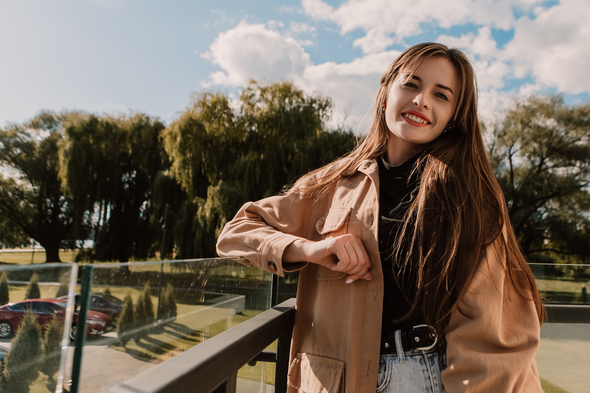 Young woman smiling while standing on a balcony with trees and sky in the background, representing comfort, confidence, and approachable women’s healthcare – obgyn north miami beach